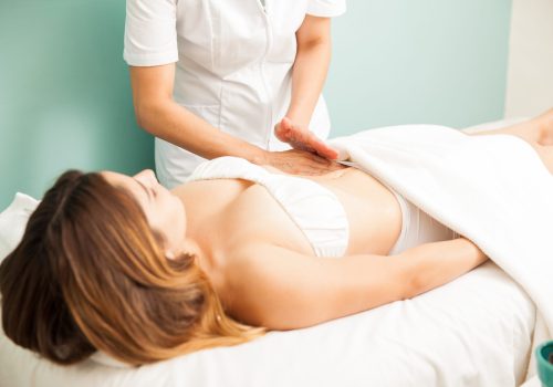 Pretty young brunette getting a lymphatic massage on her belly at a healthy and beauty spa clinic