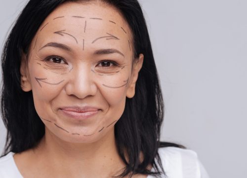 You do not need that. Healthy looking Asian lady demonstrating pre surgery guidelines on her face while smiling and standing isolated on white background